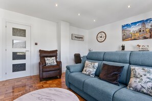 A living room with a sofa, a leather chair, a clock, and a painting on the wall. - Apartment 'Comarca Del Sella' with Mountain View and Wi-Fi (Arriondas)