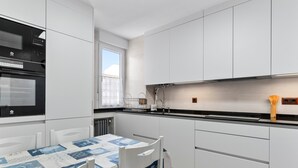 A modern kitchen with white cabinetry, a black oven, and a dining table with a blue and white tablecloth. - Apartment 'Comarca Del Sella' with Mountain View and Wi-Fi (Arriondas)