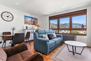 A modern living room with a sofa, chairs, a dining table, a clock, and a painting. - Apartment 'Comarca Del Sella' with Mountain View and Wi-Fi (Arriondas)