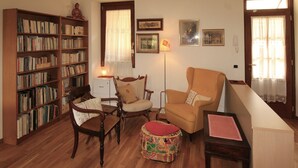 Una sala de estar con una estantería, dos sillones, un sofá, un pequeño reposapiés y una lámpara.