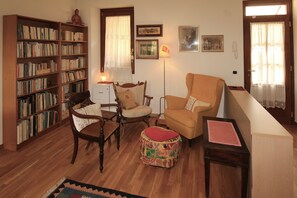 Un salon comprenant une bibliothèque, deux fauteuils, un canapé, un petit pouf et une lampe.