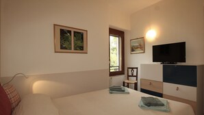 Un dormitorio con cama, televisor, cómoda y ventana.