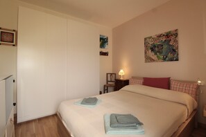 A bedroom with a bed, a nightstand, a lamp, a painting, and a wardrobe. - Apartment 'Bella' with Mountain View and Wi-Fi (Polpenazze del Garda)