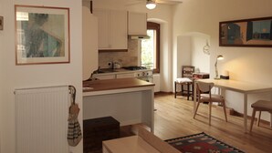 Cocina compacta con armarios blancos, encimera de madera, zona de comedor con mesa y sillas, y ventilador de techo.