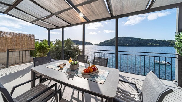 Un espacio de comedor al aire libre cubierto, con una mesa lista para dos personas, con vistas a un lago y un barco a lo lejos.