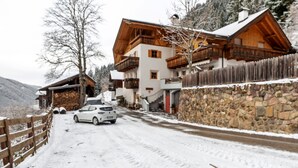 Une route enneigée menant à une maison en bois dotée de balcons et d’un mur en pierre.