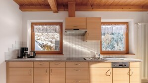 Une cuisine avec des armoires en bois, un plan de travail, une fenêtre donnant sur les arbres et une cuisinière encastrée.