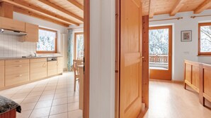 Un intérieur en bois comprenant une cuisine, un coin repas et une vue sur un paysage enneigé, visible à travers une porte.