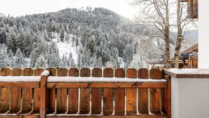 Une clôture en bois, recouverte de neige, surplombe une forêt enneigée et un bâtiment à l’extérieur en bois.