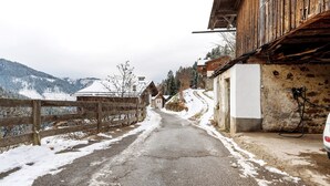 Eine verschneite Straße führt zu einem Holzhaus, vor dem ein Auto geparkt ist.