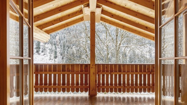 Eine Holzterrasse mit Geländer, einer Holzbeschichtung und Blick auf einen verschneiten Wald.