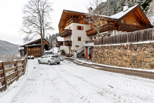 A snow-covered road leading to a wooden house with balconies and a stone wall.