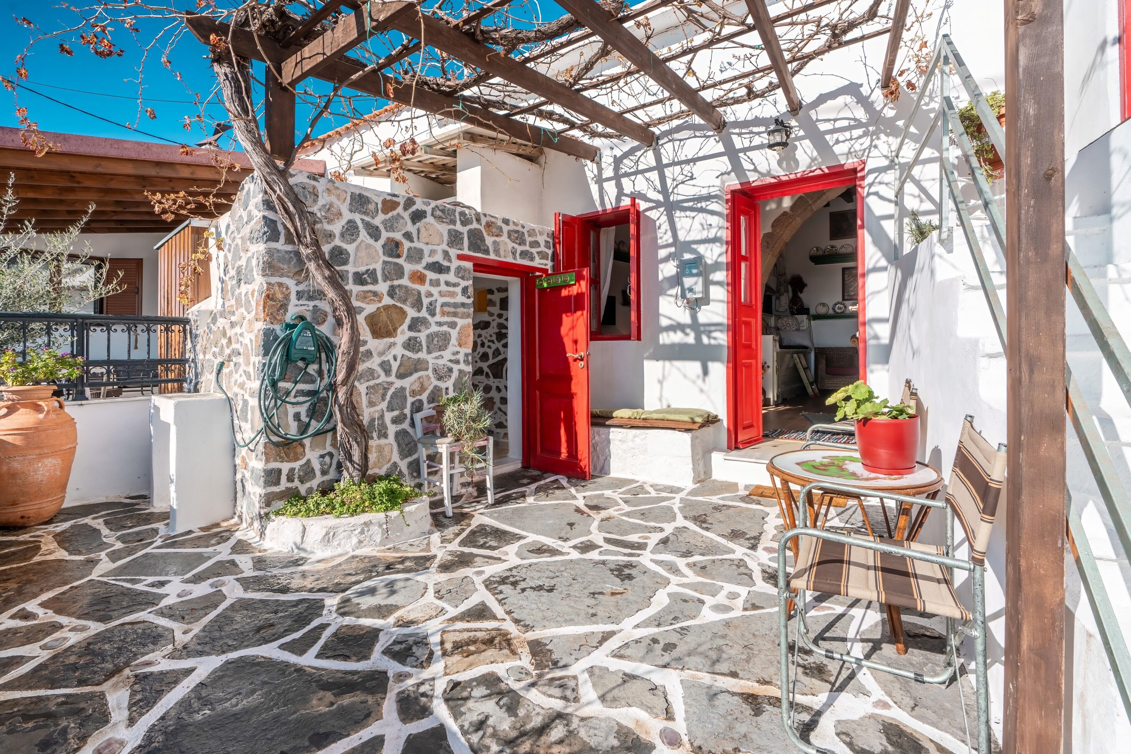 A stone-paved courtyard with a pergola, red doors, and outdoor seating.