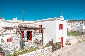 A white building with red shutters, stone walls, and a small patio with outdoor furniture. - Holiday Home 'Tis Manas' with Sea View, Private Terrace and Wi-Fi (South Rhodes)