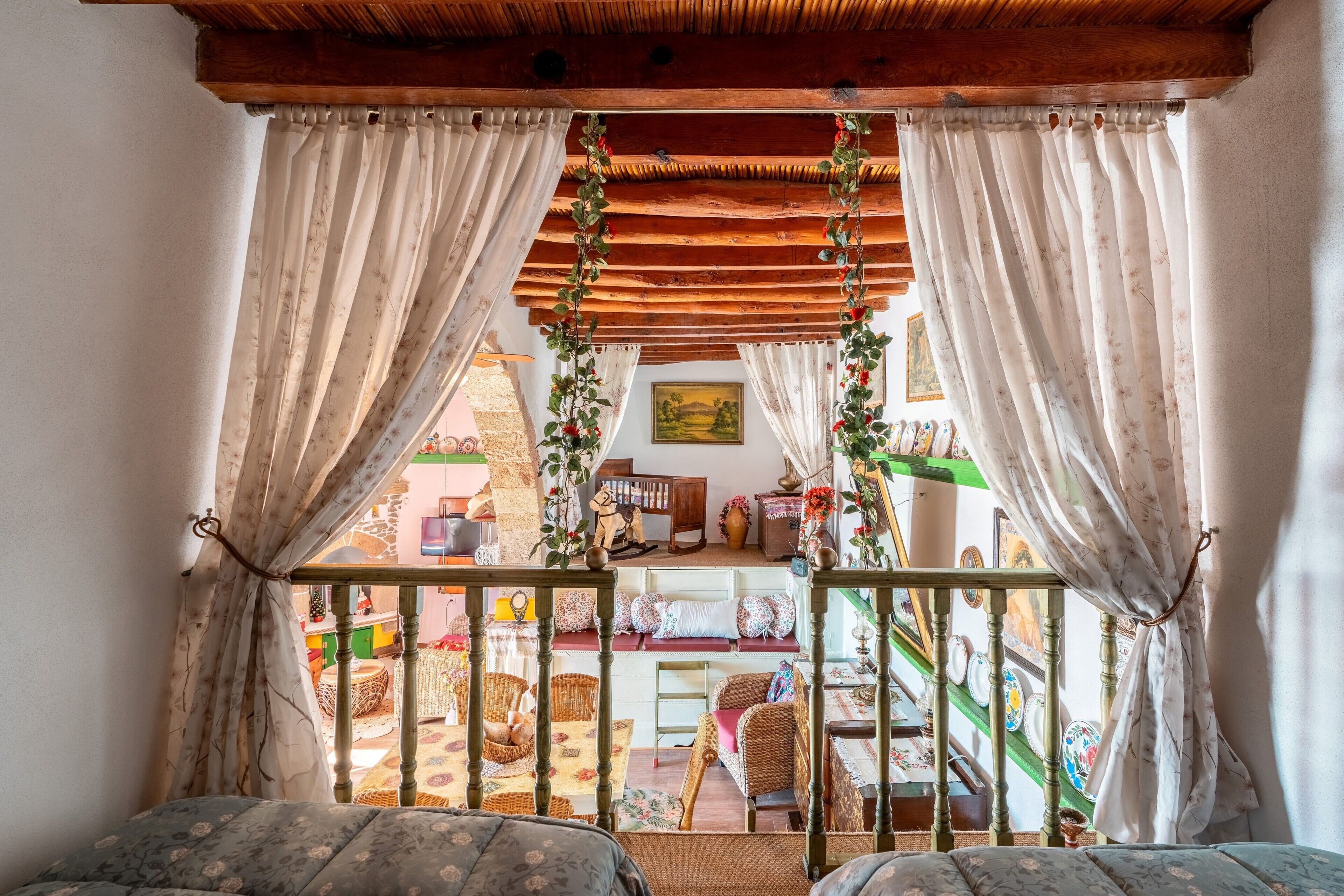 A room with a wooden ceiling, a balcony with a railing, and a view of a colorful outdoor area.