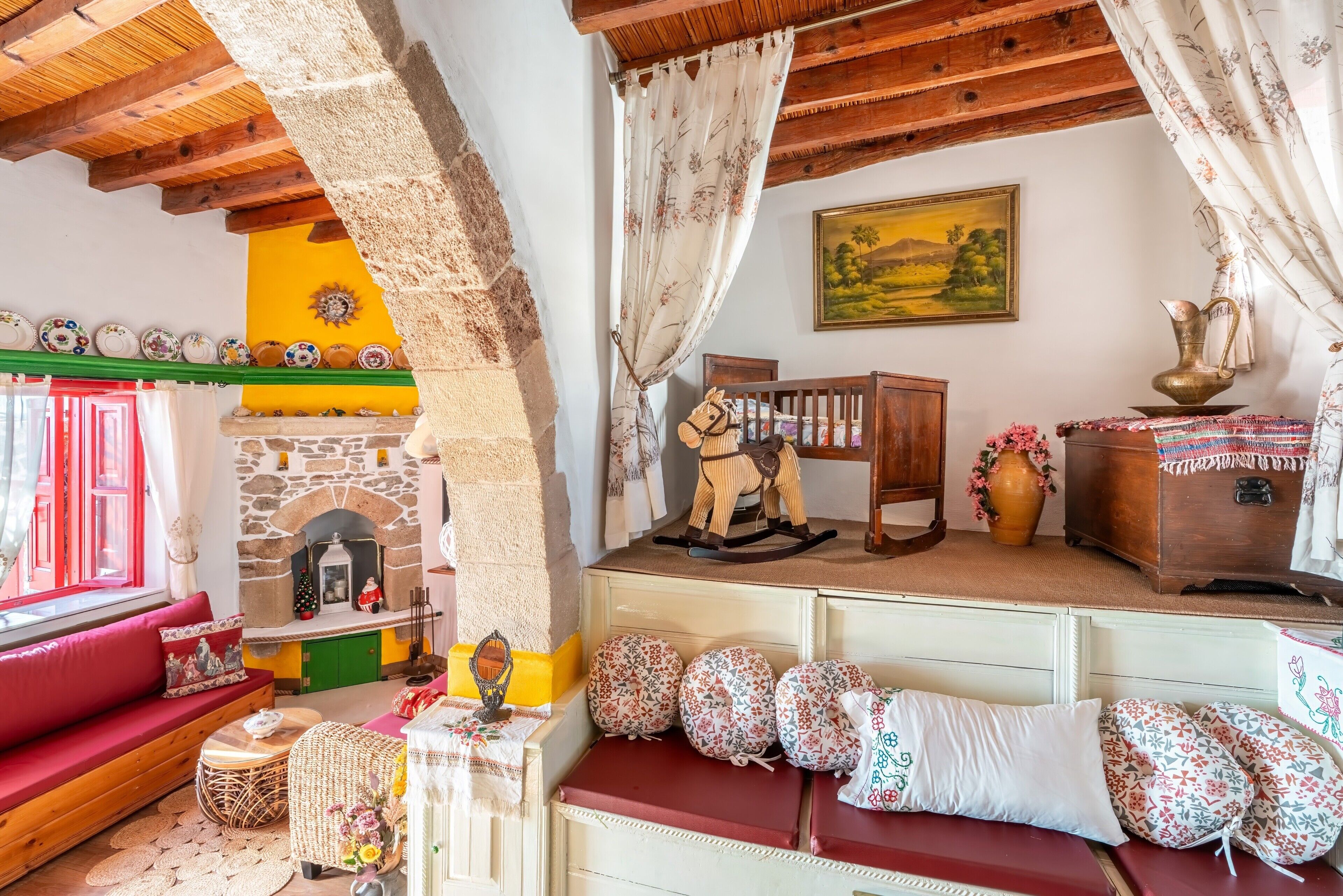 A rustic interior with a stone fireplace, wooden beams, a red sofa, and a wooden rocking horse.