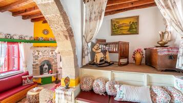 A rustic interior with a stone fireplace, wooden beams, a red sofa, and a wooden rocking horse.