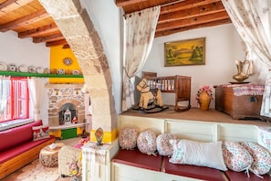 Un interior rústico con chimenea de piedra, vigas de madera, un sofá rojo y un caballo balancín de madera.