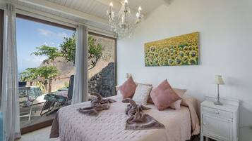 Ein Schlafzimmer mit einem großen Bett, einer Kristallleuchter, einem Gemälde und Blick auf eine felsige Landschaft durch ein Fenster.