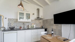 Une cuisine avec des meubles blancs, un four à micro-ondes, un évier, une table en bois et un téléviseur fixé au mur.
