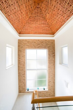 Una stanza con soffitto a mattonelle, un'ampia finestra con vetro satinato e una ringhiera in legno per la scala.