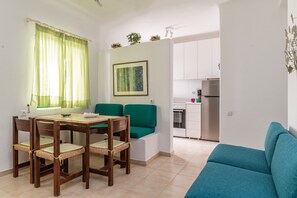 Un espace de vie compact comprenant une table à manger, des chaises, un canapé, un coin cuisine et un tableau encadré au mur.