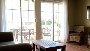Una habitación con sofá, una mesa de madera, una silla de mimbre y puertas de vidrio correderas que dan a un patio exterior.