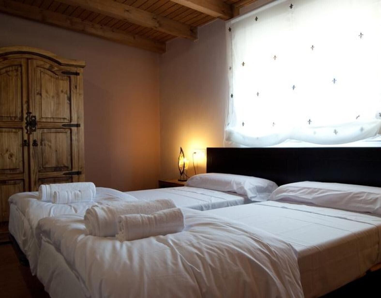 Une chambre d’hôtel avec deux lits, une armoire en bois, une table de chevet avec une lampe et une fenêtre avec un rideau.