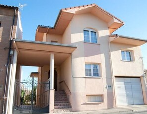 A two-story building with a covered entrance, a garage, and a staircase leading to the upper floor.