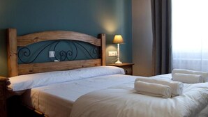 Una habitación de hotel con cabecera de madera, dos camas, una mesita de noche con lámpara y una ventana con cortinas.