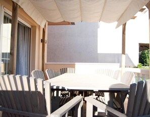 An outdoor dining area with a large table and chairs, a white umbrella, and a view of the building's exterior.