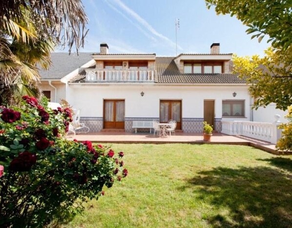A two-story house with a balcony, a front porch with a bench, and a well-maintained lawn.