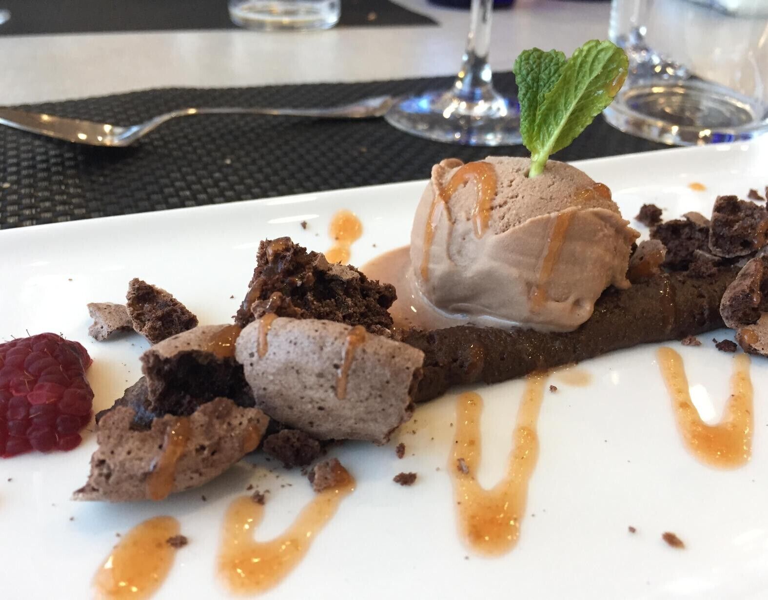 Un plato de postre con mousse de chocolate, un hilo de caramelo y frambuesas.