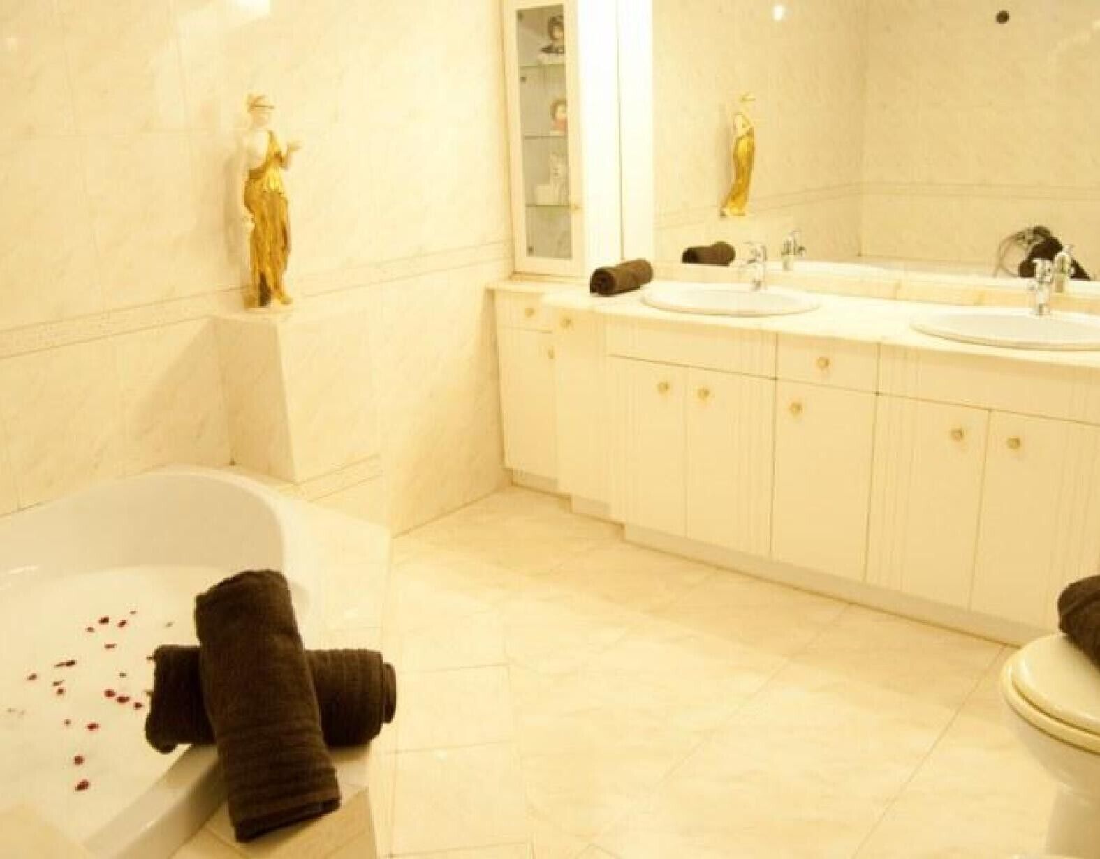 Un baño con bañera, dos lavamanos, un espejo grande y una estatua.
