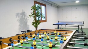 Una mesa de fútbol de mesa en una habitación con una ventana y una mesa de tenis en el fondo.
