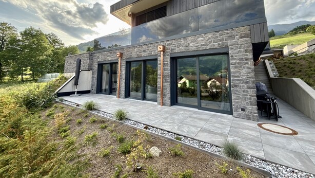 Ein modernes Haus mit einer Steinfassade, großen Fenstern und einem Satteldach.