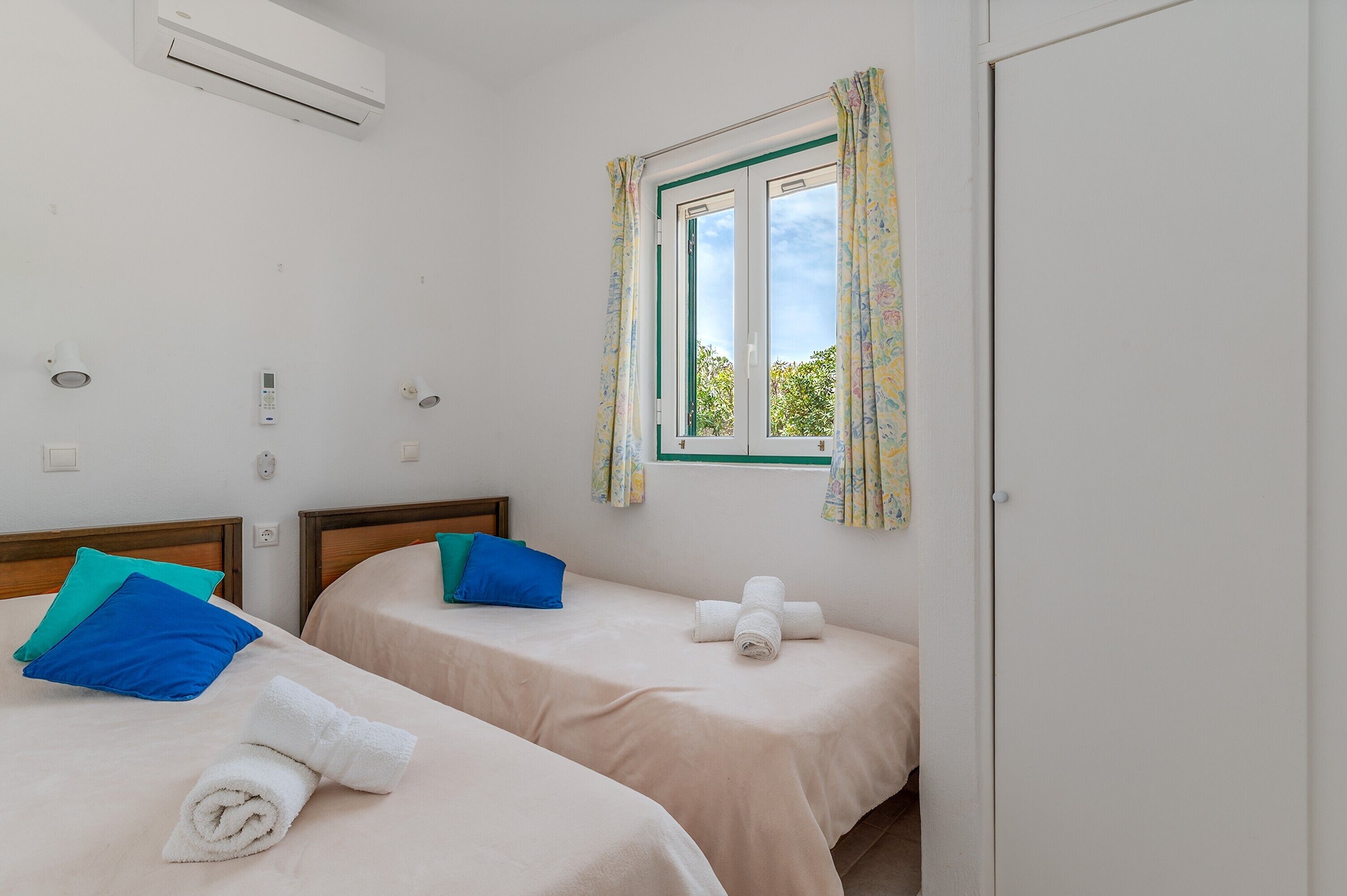 Une chambre d’hôtel avec deux lits, une fenêtre avec des rideaux, un climatiseur et un panneau de commande fixé au mur.