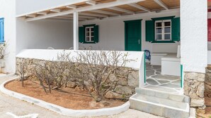 Un edificio blanco con cimientos de piedra, un porche cubierto y un pequeño jardín con árboles desnudados.