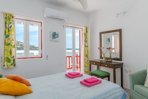 Ein Schlafzimmer mit Bett, Kissen, Schreibtisch, Stuhl, Spiegel und Meerblick.