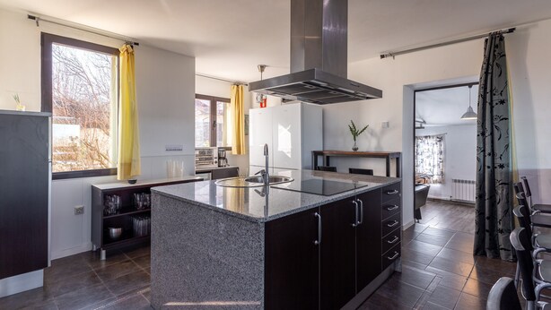 Una cocina moderna con una isla central, armarios oscuros y una campana extractora de acero inoxidable.