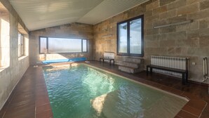Una piscina interior con paredes de piedra, ventanas amplias y un banco.