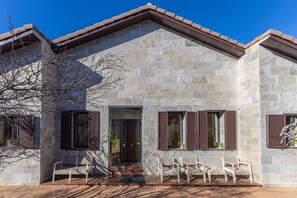 Un edificio de piedra con tejado de tejas, puerta de cristal y una zona de estar con sillas.
