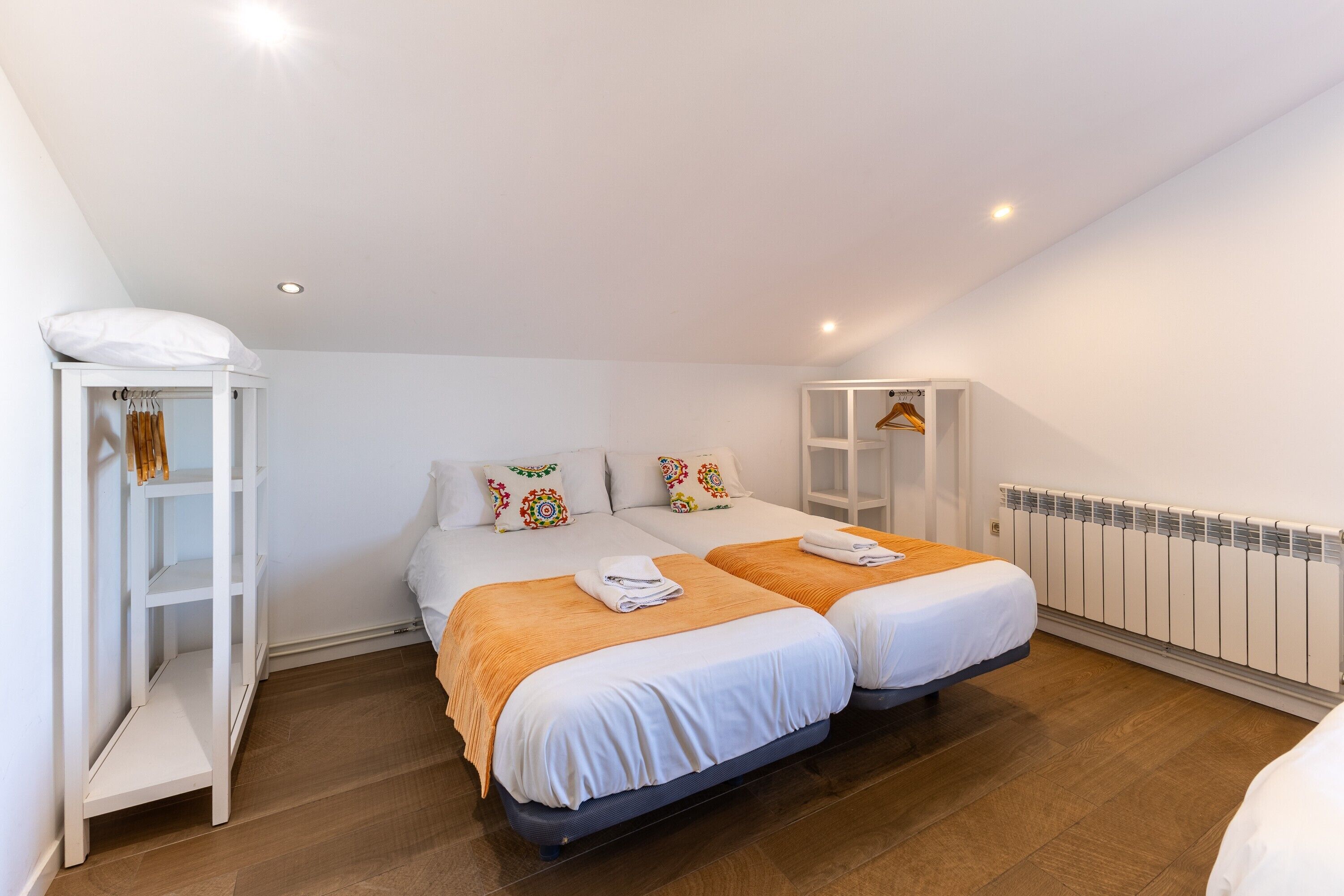 A bedroom with two beds, a wardrobe, a radiator, and a ceiling light.