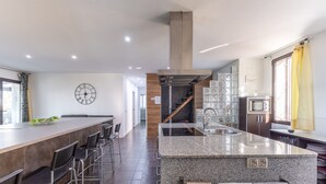 Una cocina moderna con una isla central, taburetes de bar, un reloj y una escalera que lleva a un altillo.