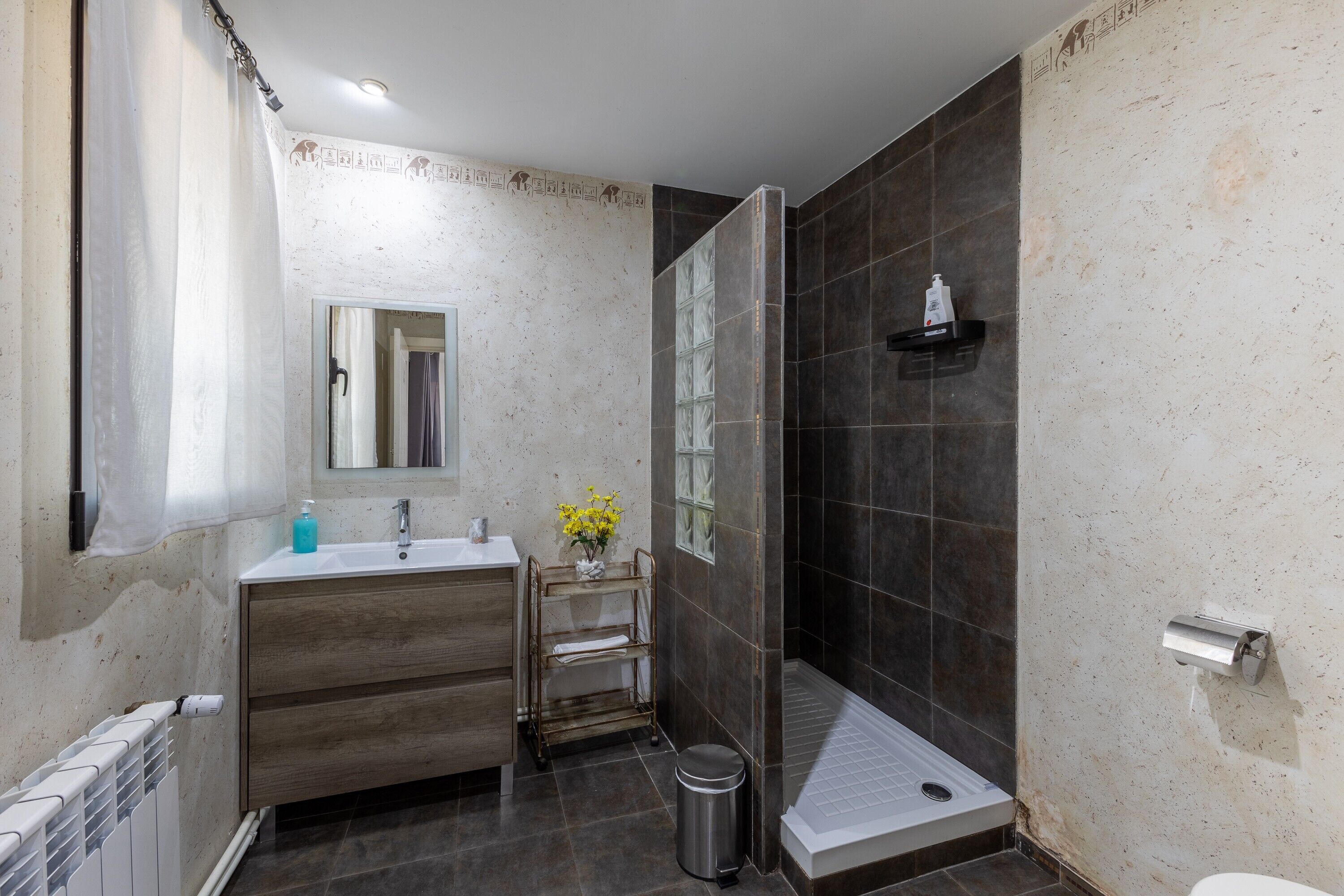 Een badkamer met een douche, een wastafel, een spiegel en een klein plankje met toiletartikelen.