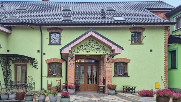 A green building with a tiled roof, a central entrance with a decorative arch, and multiple potted plants around the entrance. - 2 bedroom beautiful apartment in Obryta (Obryta)