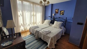 A bedroom with two beds, a chandelier, a table with a lamp, and a window with curtains. - Casa Rural El Camino, Molinaseca, El Bierzo – Mountain Views & Terrace (Molinaseca)