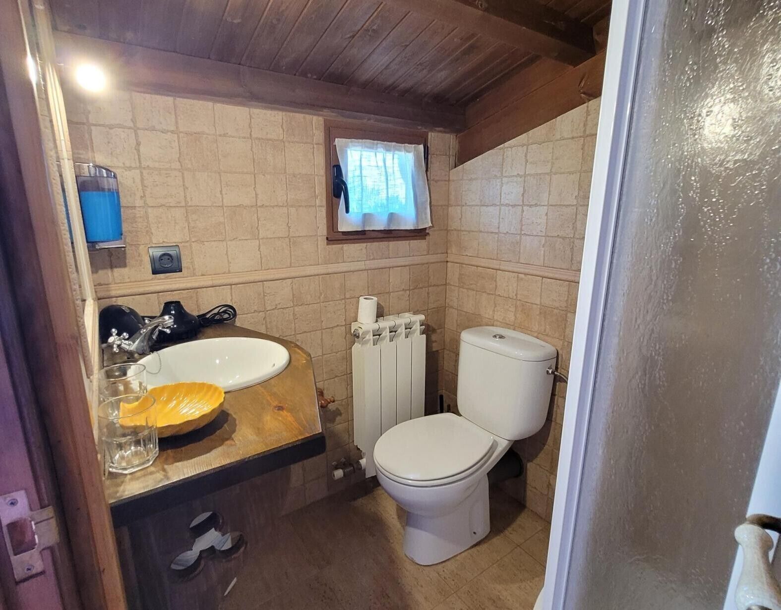 Ein Badezimmer mit einem hölzernen Waschtisch, einem weißen Waschbecken, einer Toilette und einem Fenster mit Vorhang.