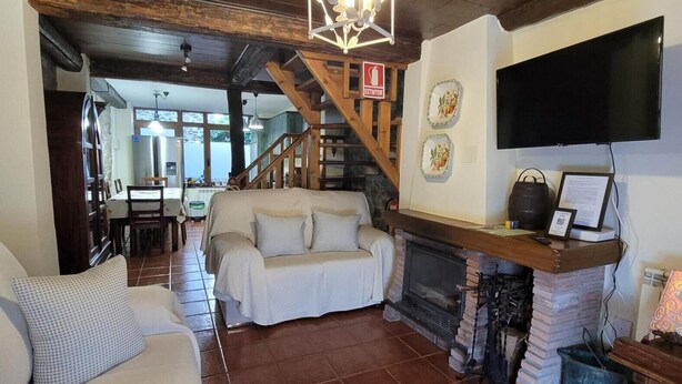 A cozy living room with a fireplace, a sofa, a TV, and a staircase leading to another room. - Casa Rural El Camino, Molinaseca, El Bierzo – Mountain Views & Terrace (Molinaseca)