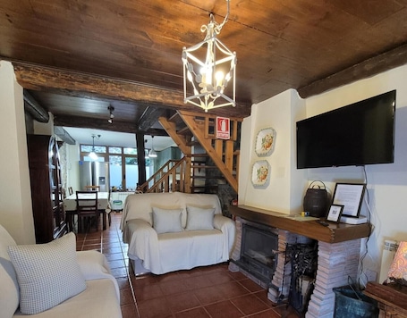 A cozy living room with a fireplace, a sofa, a TV, and a staircase leading to another room.